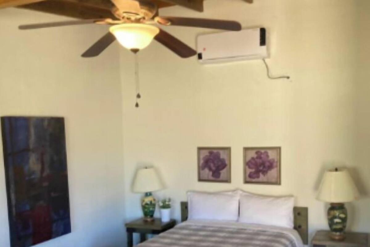 Quarto com uma cama, um banquinho, um ventilador de teto e duas luminárias de parede.