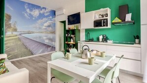 Una cocina moderna con una pared verde de acento, un área de comedor con una mesa blanca y sillas verdes, y un ventanal con vista a una masa de agua.