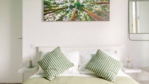 Un dormitorio con una cama, dos almohadas, una mesita de noche y un cuadro en la pared.