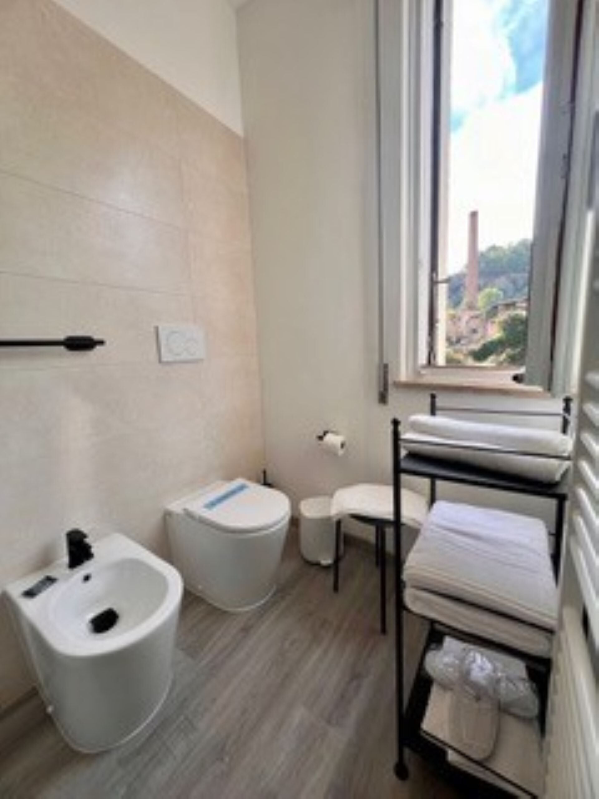Een badkamer met een bidet, toilet en een raam met uitzicht op een gebouw.