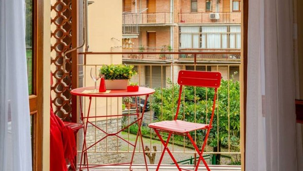 A balcony with a red chair and table, a view of a residential building, and a wooden lattice partition.