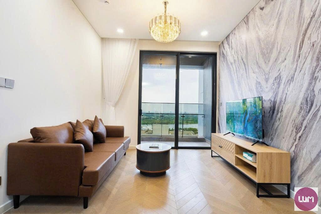 A modern living room with a brown sofa, a round coffee table, a TV on a wooden stand, and a large window with a view.