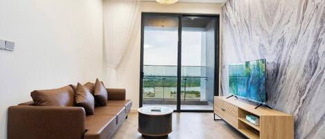 A modern living room with a brown sofa, a round coffee table, a TV on a wooden stand, and a large window with a view.