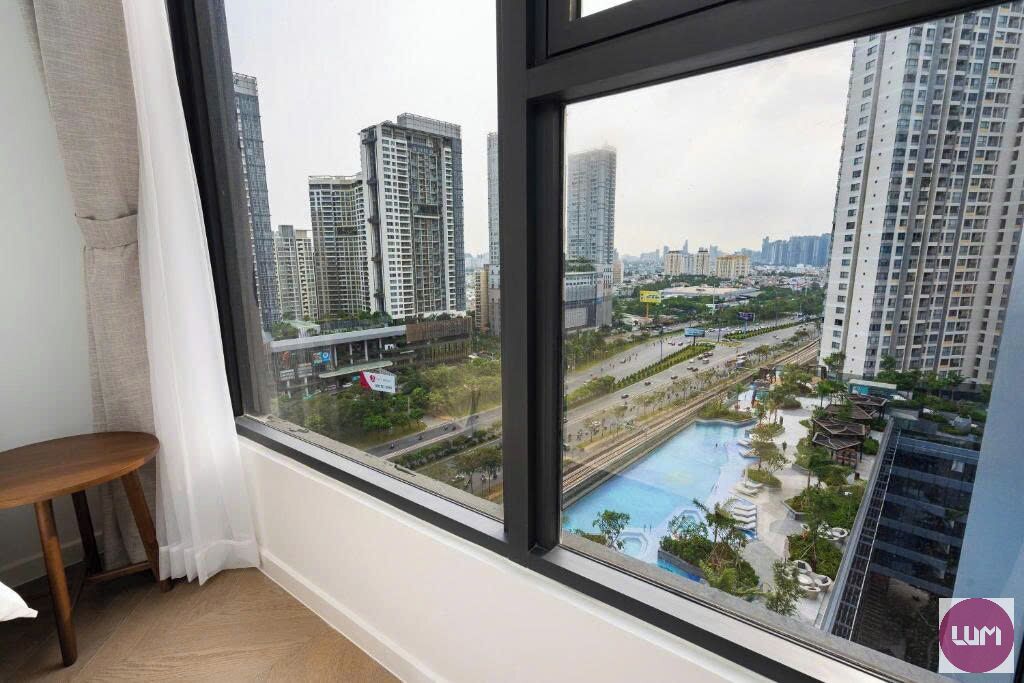 A room with a large window overlooking a cityscape, including high-rise buildings and a swimming pool.