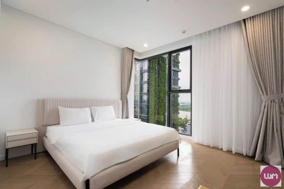 A modern bedroom with a large bed, a nightstand, and a window with curtains.