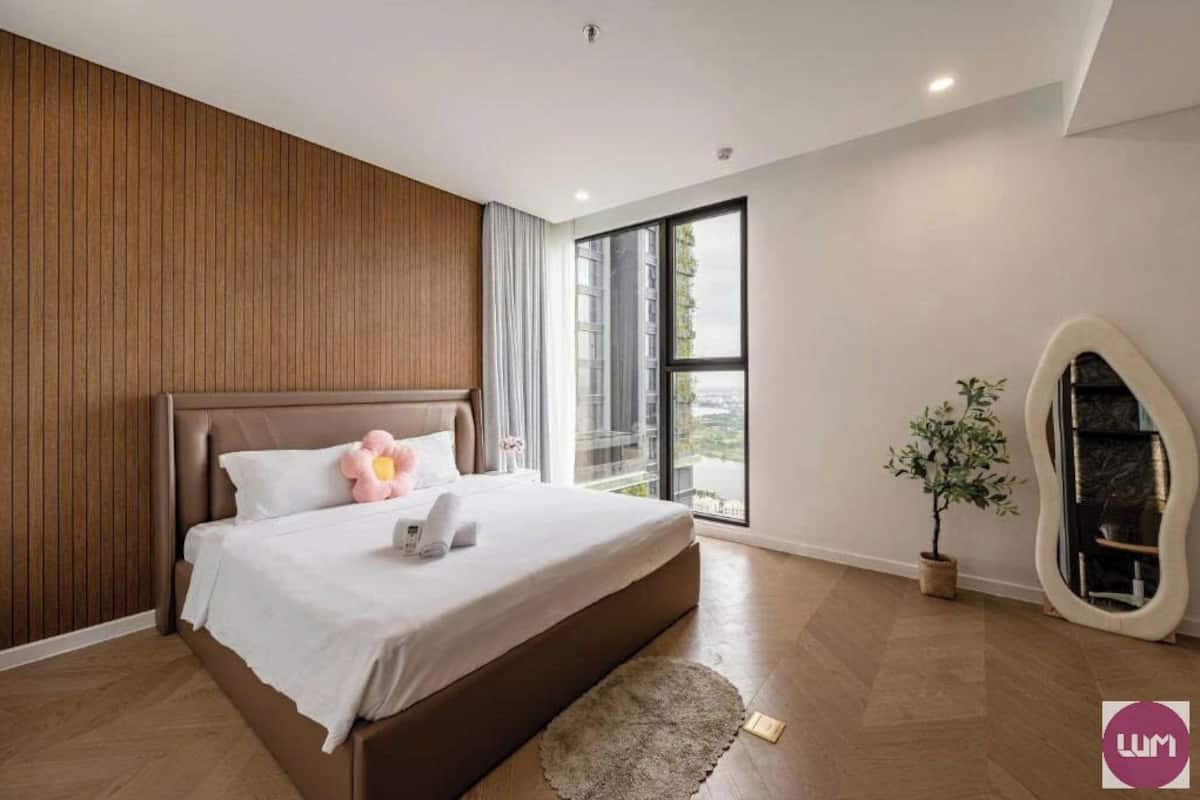 A modern bedroom with a large bed, a wooden panel wall, a large window, and a small plant.