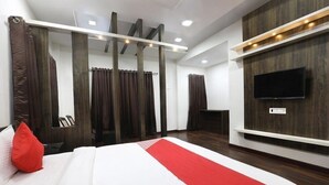 A modern hotel room with a large bed, a flat-screen TV mounted on the wall, and a wooden accent wall. - Vishnupriya Grand (Kolhapur)