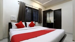 A bedroom with a bed, a wardrobe, a window with curtains, and a thermostat on the wall. - Vishnupriya Grand (Kolhapur)