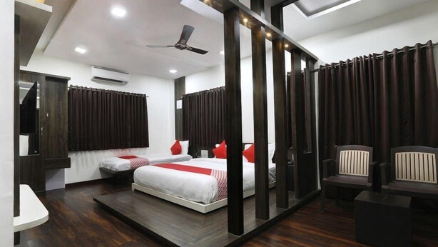 A modern hotel room with two beds, a ceiling fan, and a seating area with chairs. - Vishnupriya Grand (Kolhapur)