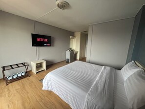 Quarto de hotel com cama, televisão fixada na parede, secretária pequena e sapateira.
