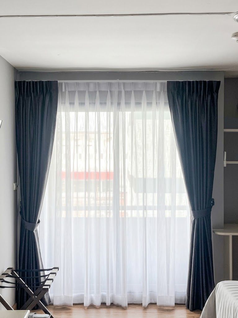 A room with a large window, curtains, a bed, and a small table.