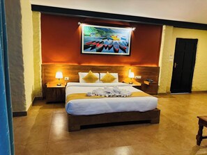 A hotel room with a large bed, two bedside tables with lamps, a painting of boats on the wall, and a door to the right. - Annapurna Boutique Hotel (Pokhara)