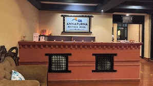 A reception desk with a sign for Annapura Boutique Hotel, a cushioned sofa, and a decorative wall with a window.