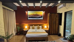 A hotel room with a bed, two bedside tables with lamps, a large painting on the wall, a wardrobe, and a potted plant.