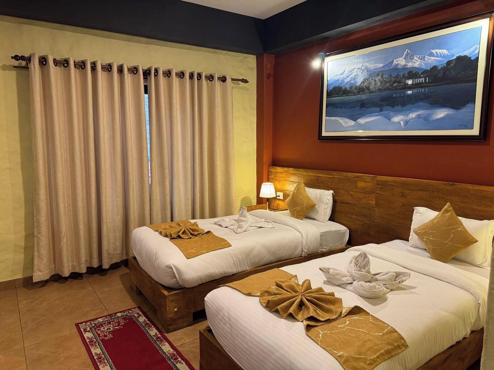 A hotel room with two beds, a red carpet, a painting of a mountain landscape, and a window with curtains.