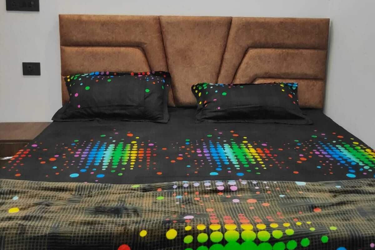 A bedroom with a brown upholstered headboard, a black bedspread with colorful dots, and two black pillows with colorful dots.