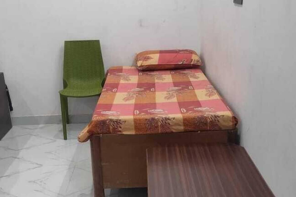 A small, sparsely furnished room with a bed, a bench, and a green chair.