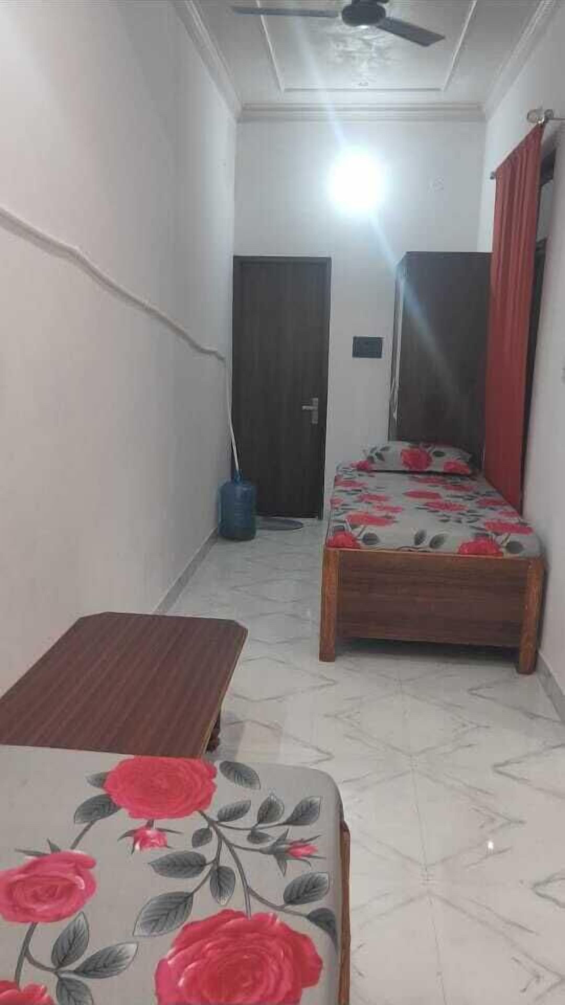 A narrow hallway with a bed featuring a floral bedspread, a wooden table, and a ceiling fan.