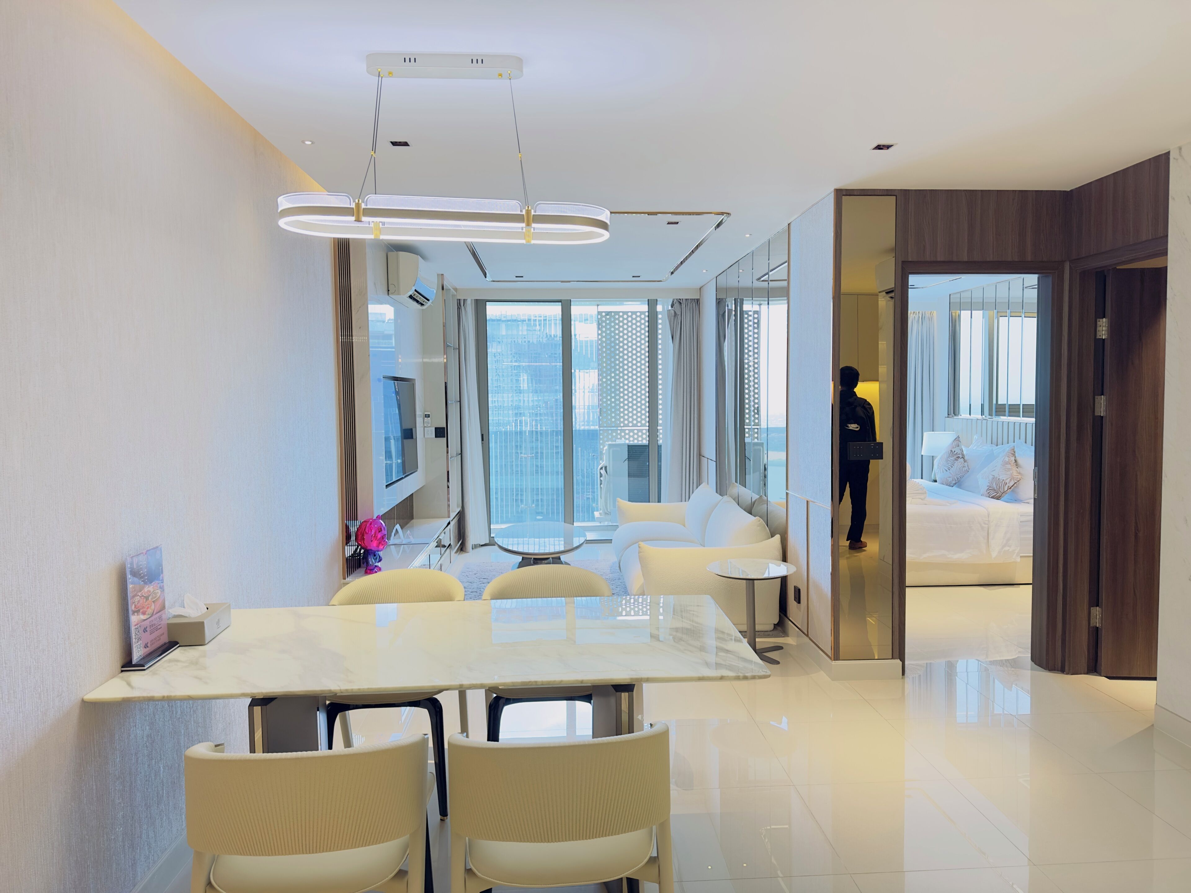 Une chambre d’hôtel moderne avec un coin repas, un lit avec une literie blanche et une vue sur le paysage urbain.