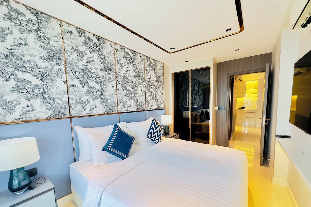 A modern hotel room with a large bed, a nightstand, a wall-mounted artwork, and a walk-in closet.