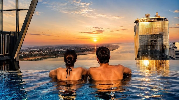 Una pareja en una piscina infinita con un paisaje urbano y un edificio moderno al fondo.