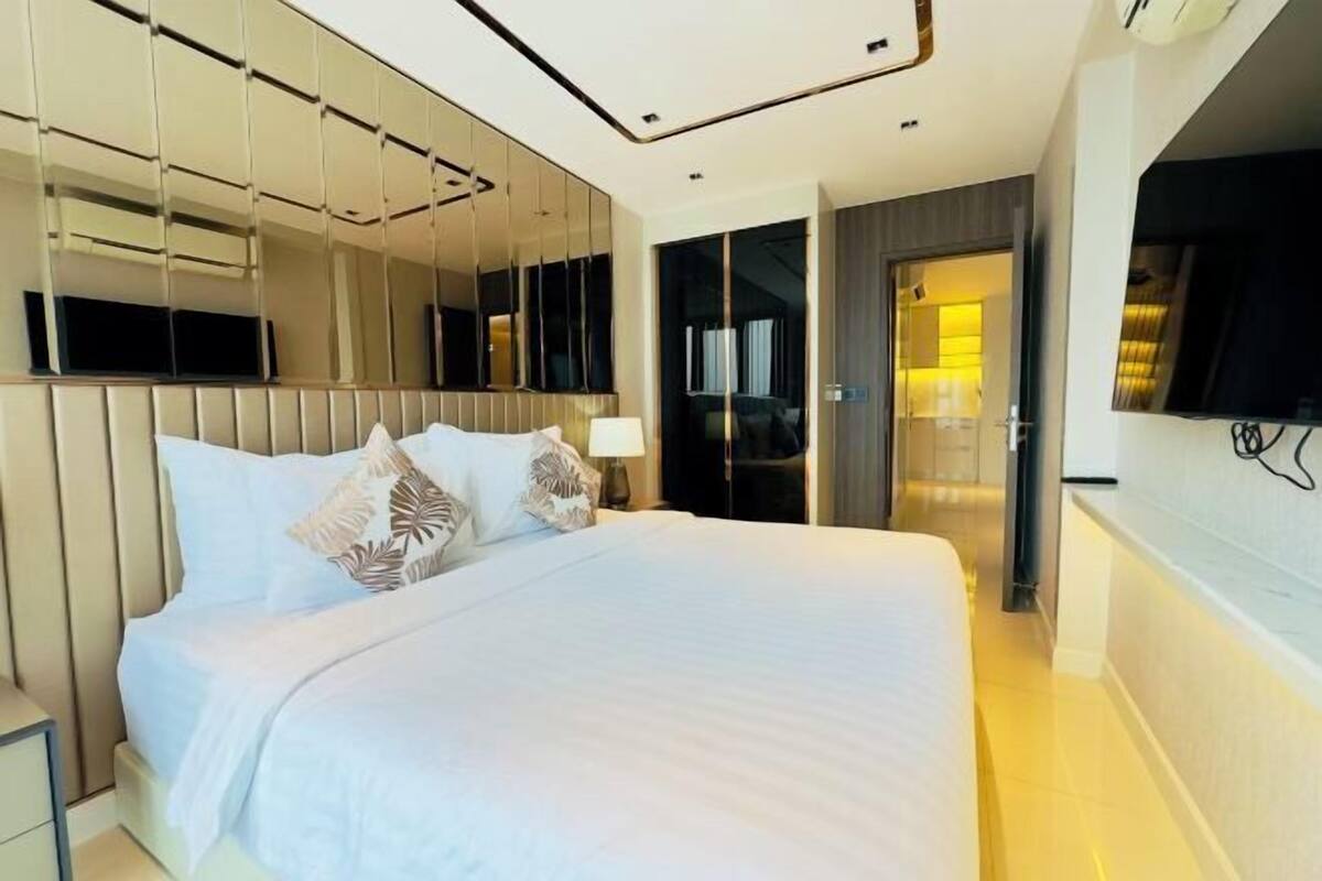 A modern hotel room with a large bed, a TV mounted on the wall, and a mirror reflecting the room.