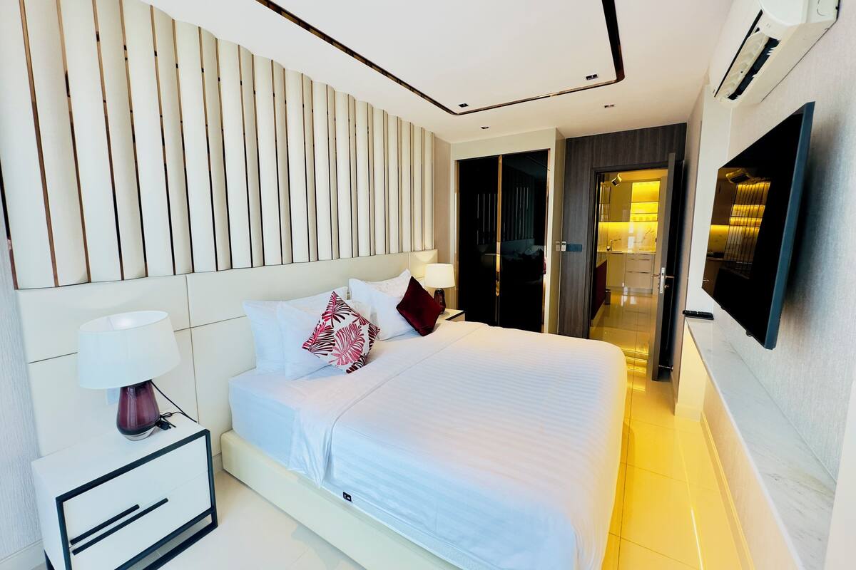 A modern hotel room with a large bed, bedside tables, a TV, and a walk-in closet.