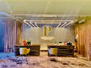 Een receptiebalie met een groot 'P'-logo, twee stoelen, een houten wand en een marmeren vloer.