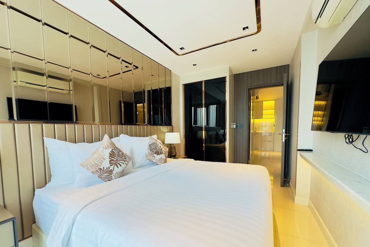 A modern hotel room with a large bed, a mirror, a TV, and a walk-in closet.