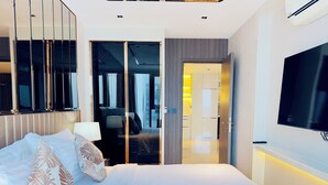 Una habitación de hotel moderna con una cama grande, un televisor, una puerta corredera al baño y vistas a la ciudad.