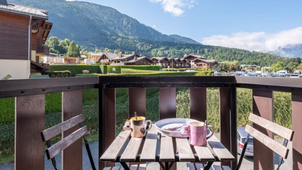 Um deck de madeira com mesa, cadeiras e uma vista panorâmica das montanhas.