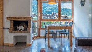 Um quarto aconchegante com lareira, mesa de jantar, cadeiras e vista para as montanhas.