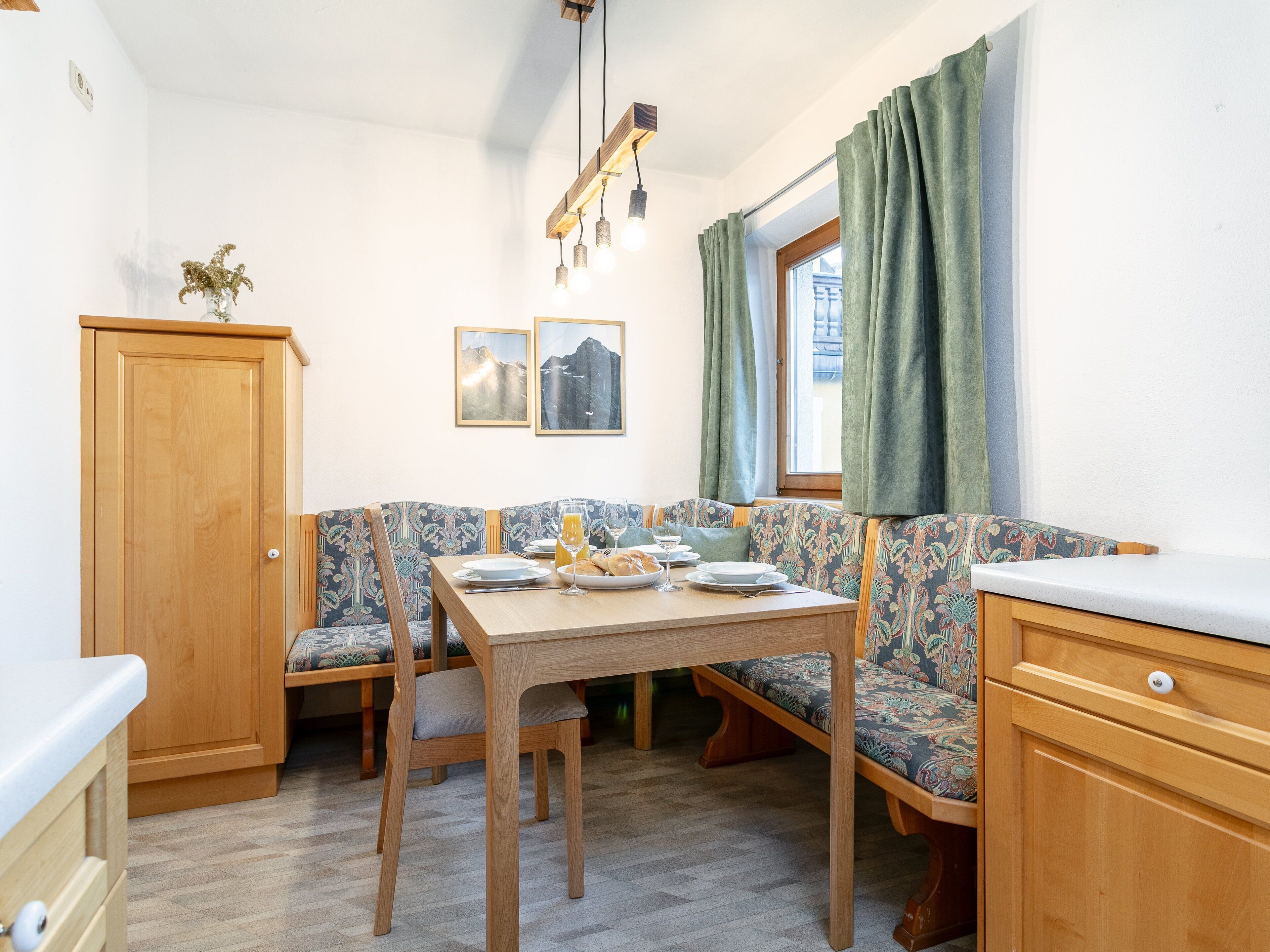 A compact kitchen with a wooden table, bench seating, and a cabinet.