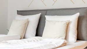 A neatly made bed with white linens and pillows, a grey upholstered headboard, and a geometric wall design. - Spacious apartment in the center, garden & sauna (Kirchberg in Tirol)