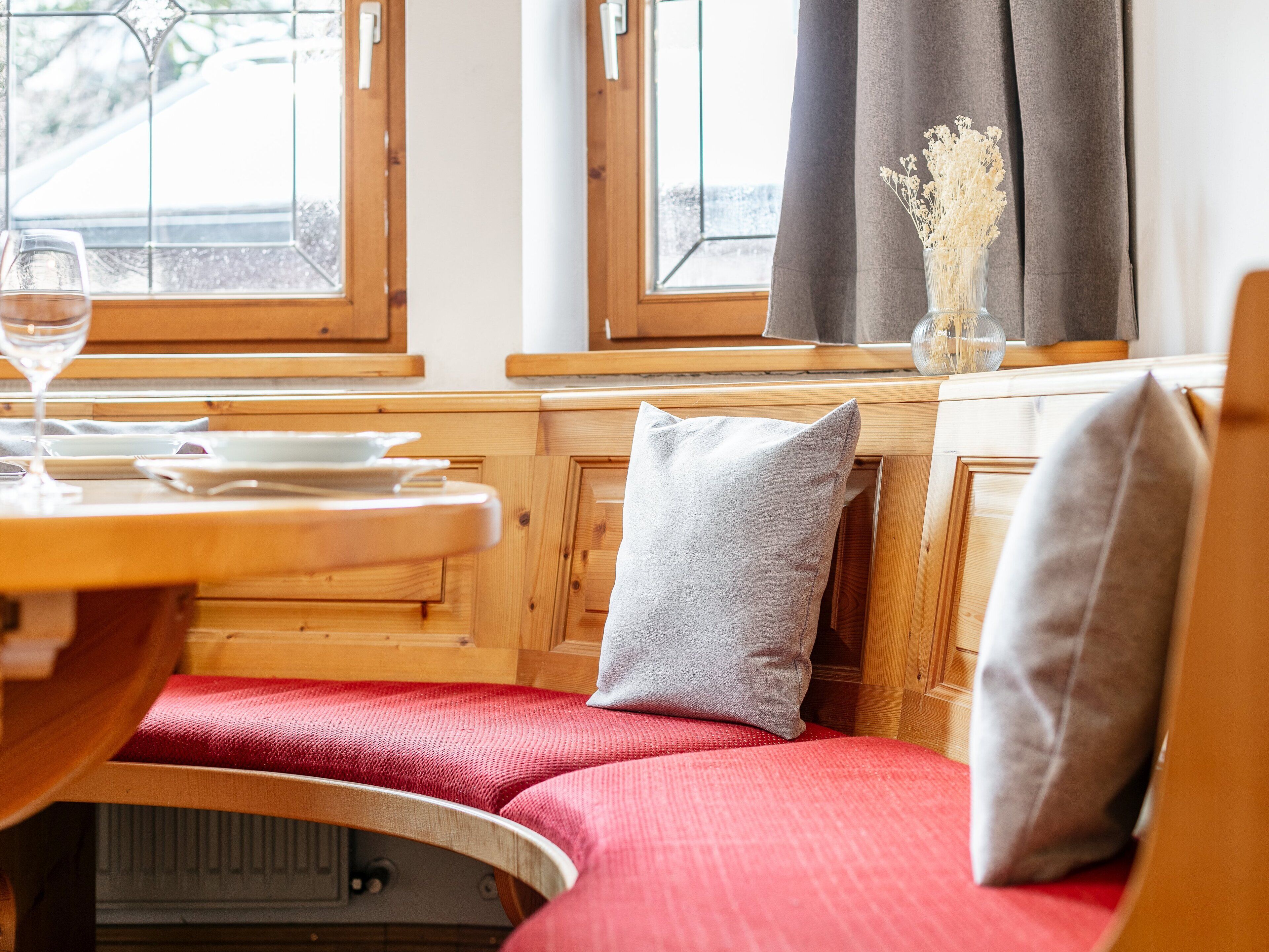 L’intérieur chaleureux d’un chalet avec des murs en bois, une table à manger avec des assiettes et un verre de vin, et un banc agrémenté de coussins.