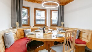 A wooden dining table with benches, a bottle of wine, and glasses. - Spacious apartment in the center, garden & sauna (Kirchberg in Tirol)