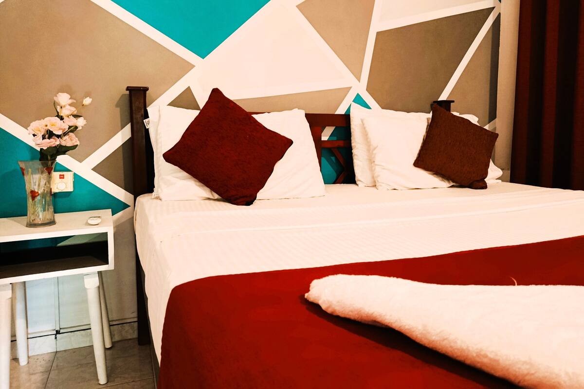 Una camera d'albergo con un letto, un comodino e un vaso con fiori.