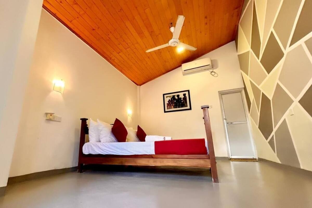 Camera da letto con soffitto in legno, un letto con biancheria rossa e bianca, una ventola a soffitto e un condizionatore d'aria a parete.