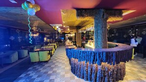 A bar area with a unique tree stump design, seating with cushions, and a patterned floor. - HSR Hotels & Resorts (Dehradun)