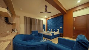 A modern hotel room with a blue upholstered sofa set, a bed with a tufted headboard, a ceiling fan, and wooden paneling. - HSR Hotels & Resorts (Dehradun)