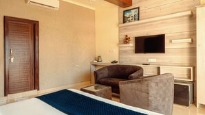 A modern hotel room with a wooden wall, a flat-screen TV, a sofa, a coffee table, and a bed. - HSR Hotels & Resorts (Dehradun)
