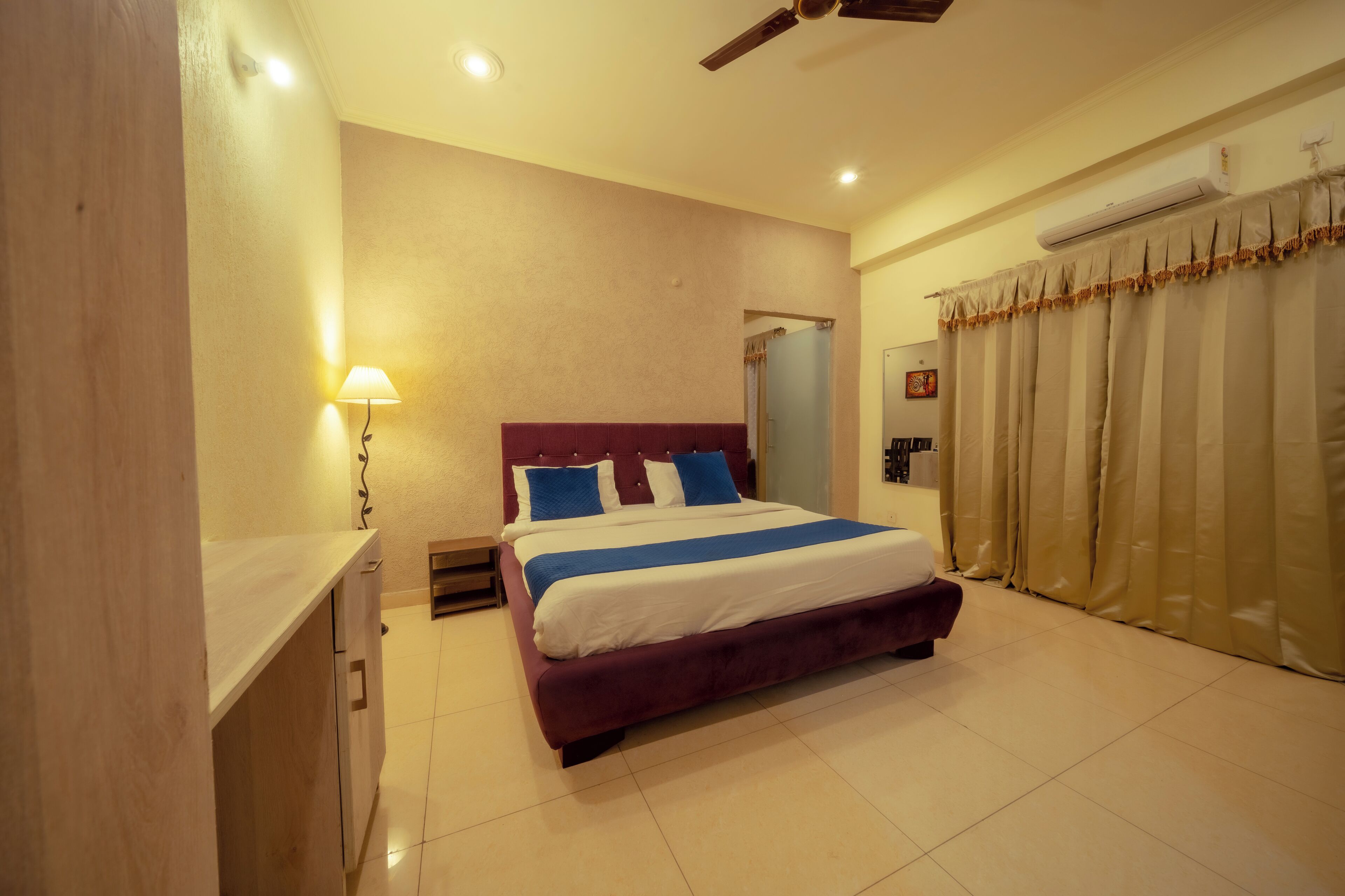 A bedroom with a bed, a nightstand, a lamp, a ceiling fan, and a window with curtains.