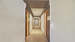 A long, narrow hallway with a tiled floor and wooden doors on either side. - Hotel Anugraha Deluxe (Kolhapur)