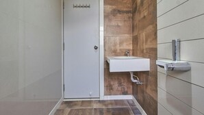 A bathroom with a white door, a sink with a mirror, and a tiled floor. - Hotel Anugraha Deluxe (Kolhapur)