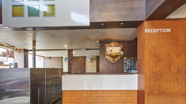A reception area with a wooden reception desk, a wall-mounted decorative piece, and a sign labeled "RECEPTION". - Hotel Anugraha Deluxe (Kolhapur)