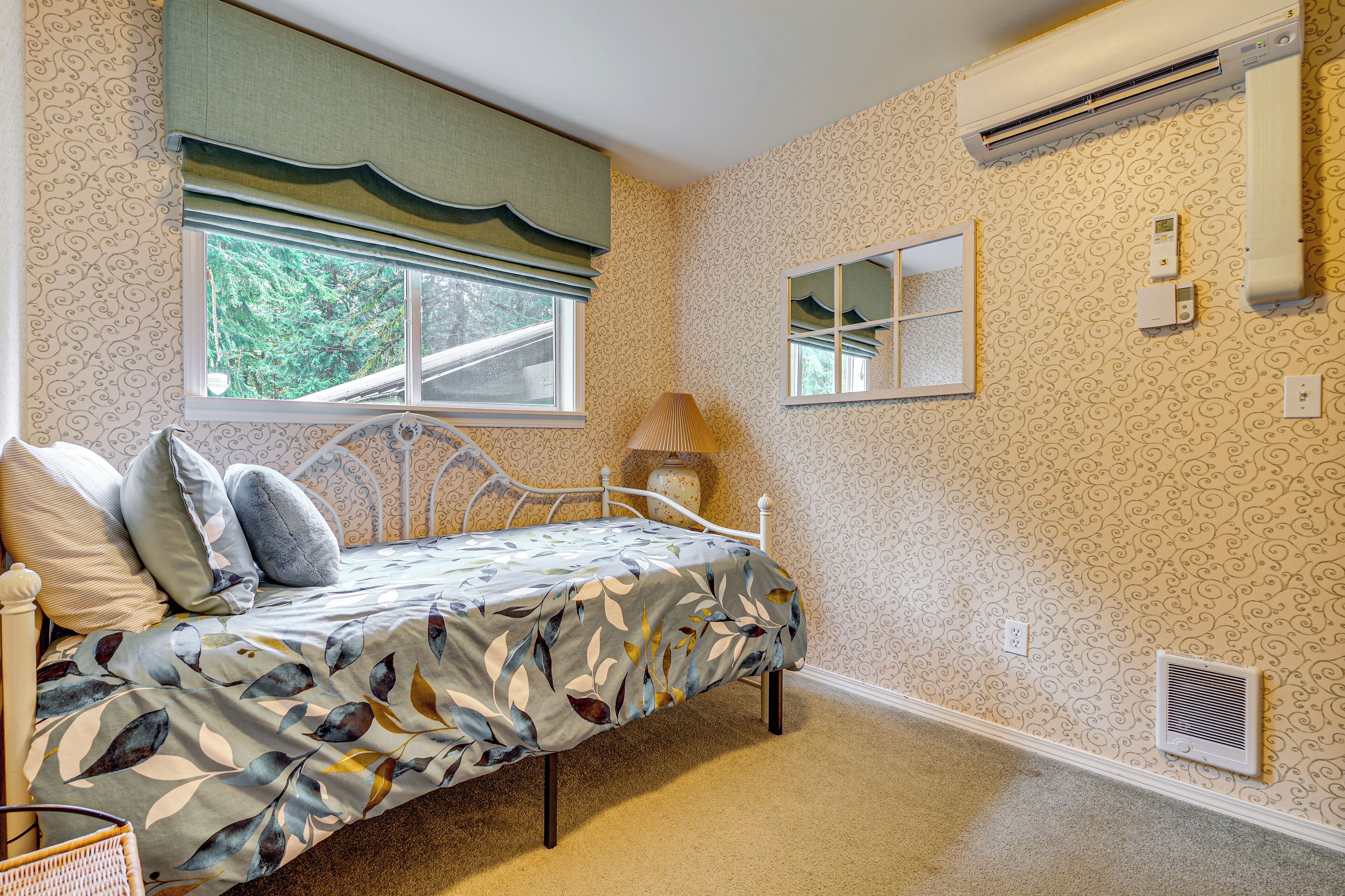 A bedroom with a bed, window, mirror, and wall-mounted air conditioning unit.
