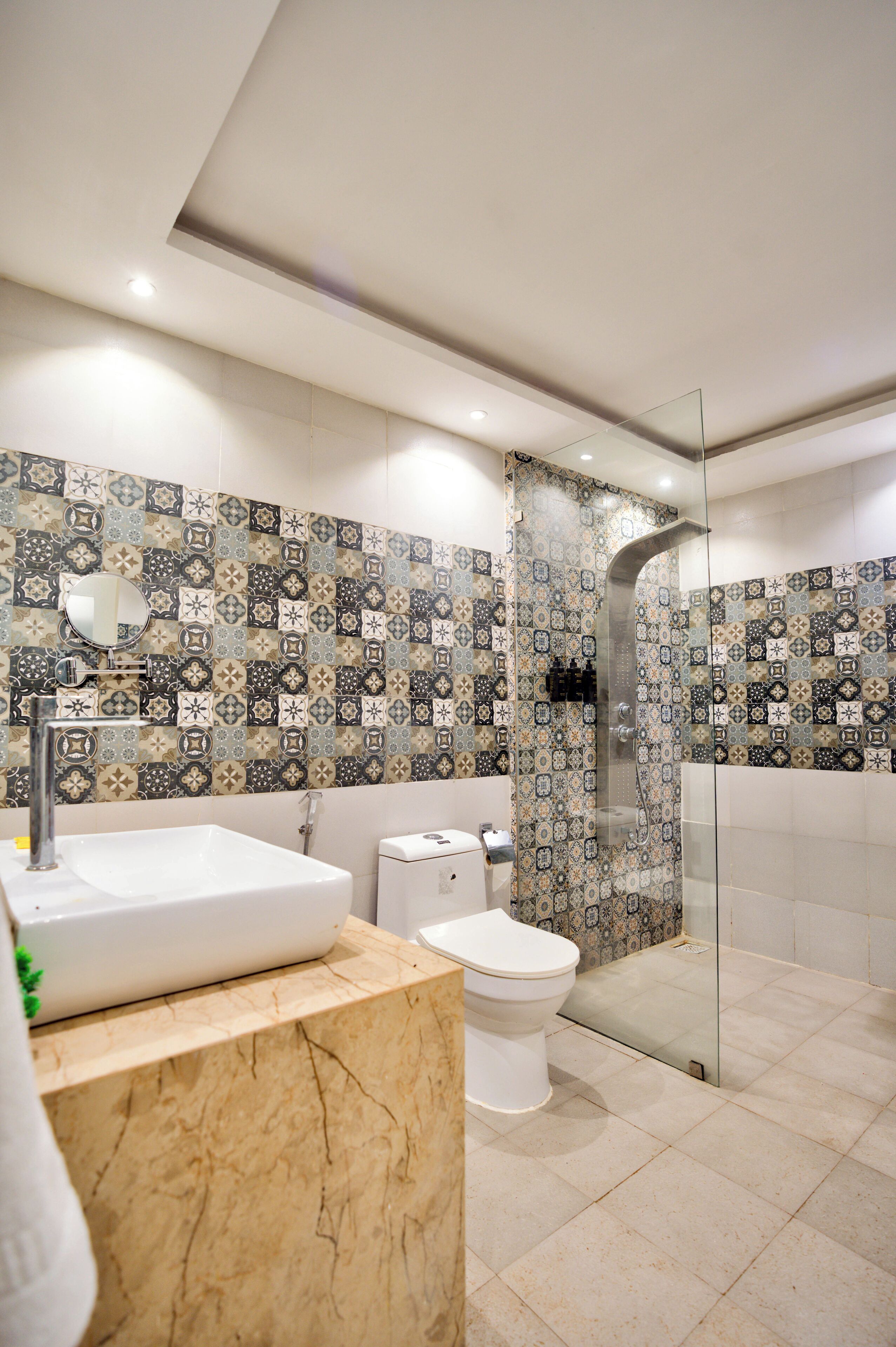 A modern bathroom with a patterned tile backsplash, a white sink, a toilet, and a glass-enclosed shower area.