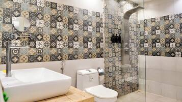 A modern bathroom with a patterned tile backsplash, a white sink, a toilet, and a glass-enclosed shower area.