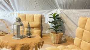 A cozy interior with a yellow sofa, a small table with a lantern, and a potted plant. - Khaopoon Camping (Kanchanaburi)