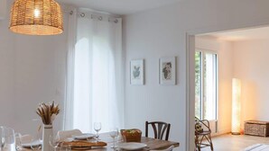 A dining area with a wooden table, white chairs, and a hanging light fixture. - Ty Mezou - Pretty house on the Gr34 near to the se (Porspoder)